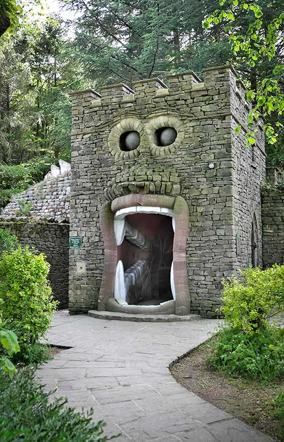 Stone castle tower styled to look like a giant monster's face, with two dark round windows serving as eyes and a large open mouth acting as a tunnel entrance.