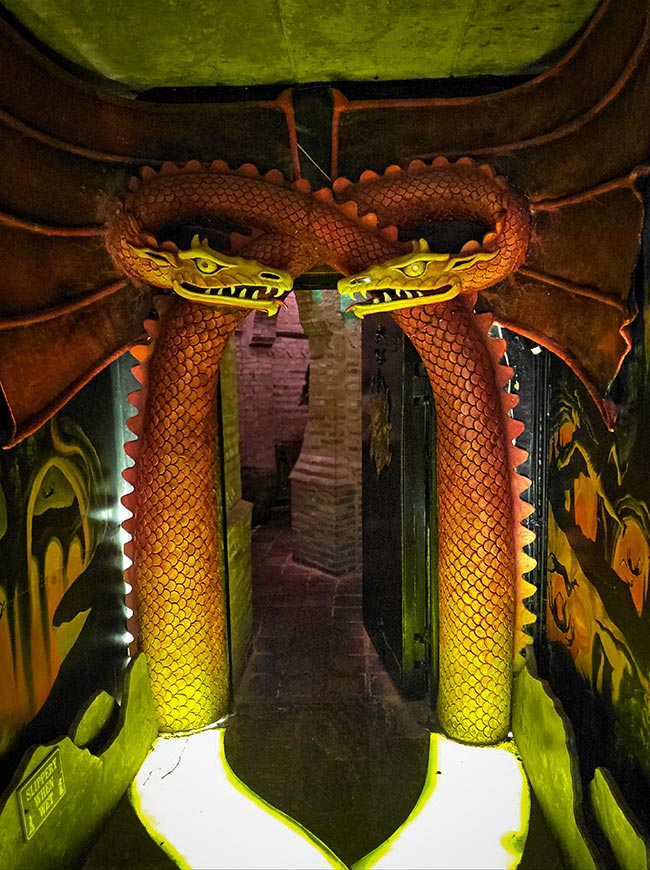 The image shows a striking, brightly colored twin-dragon archway inside the labyrinth at The Forbidden Corner in Tupgill Park, North Yorkshire